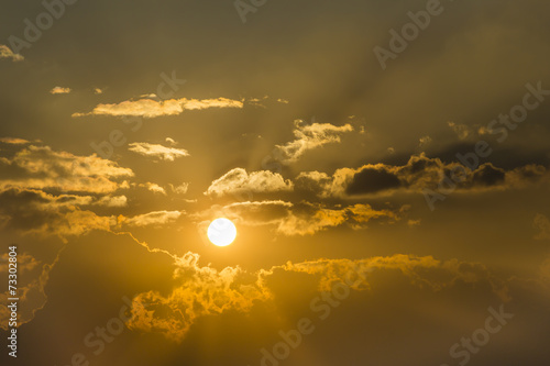 bright sun in an orange sky with dark clouds at sunset