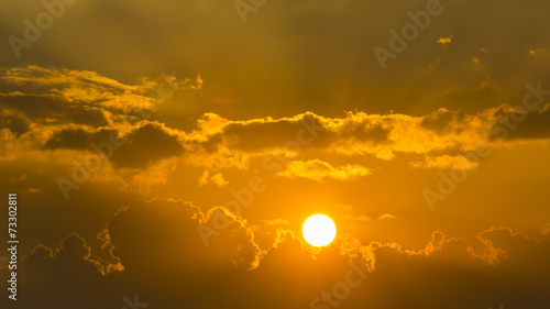 bright sun in an orange sky with dark clouds at sunset