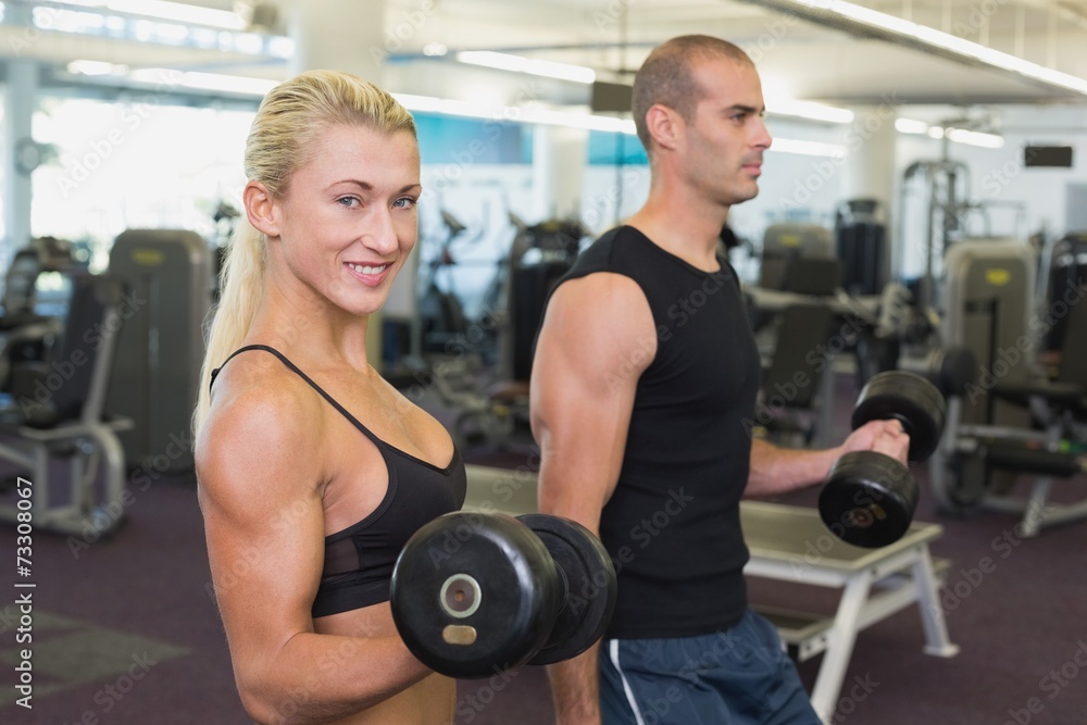 Couple exercising with dumbbells in gym Couple exercising with dumbbells in gym
