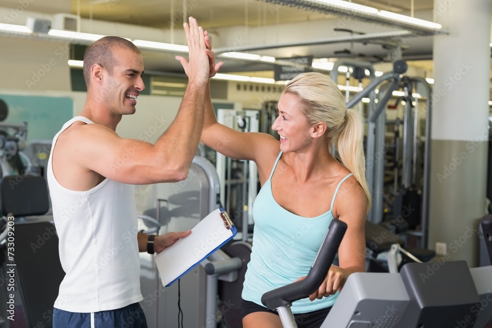 Trainer giving high five to his client on exercise bike at gym Trainer giving high five to his client on exercise bike at gym