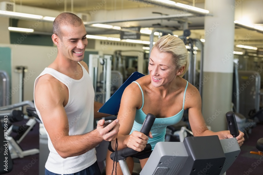 Trainer timing his client on exercise bike at gym Trainer timing his client on exercise bike at gym