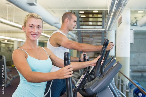 Side view of a fit young couple working on x-trainers at the gym