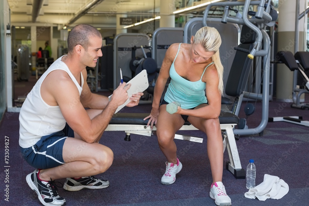 Male trainer assisting woman with dumbbell in gym Male trainer assisting woman with dumbbell in gym