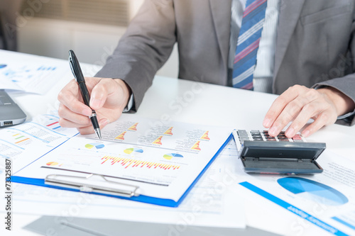 Businessman analyzing report on chart with laptop and calculator