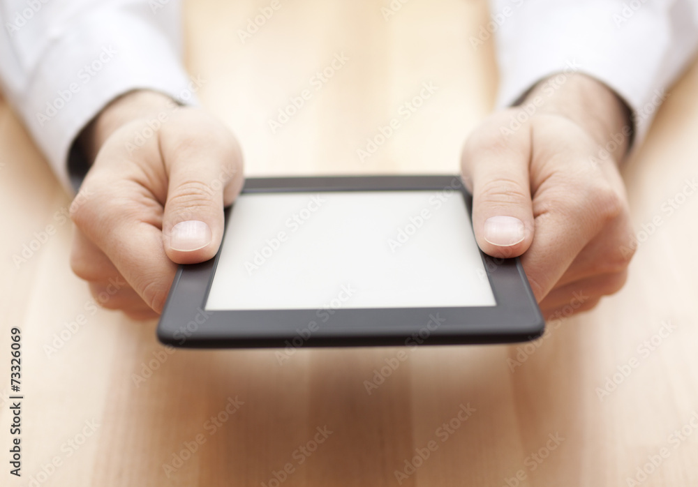 Tablet or e-book reader in hands on wood background