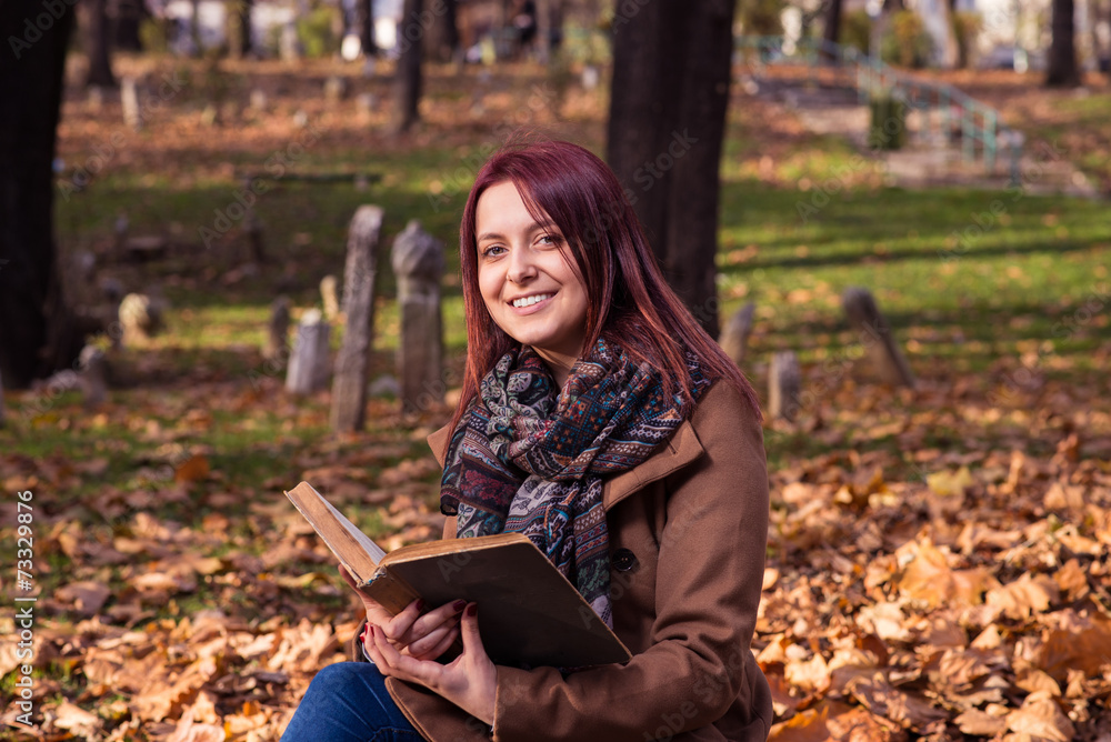 Obraz premium redhead girl sitting on bench in park and reading book