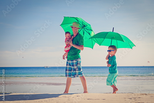 father and kids with umbrellas on beach vacation
