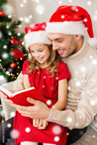 smiling father and girl in santa hats reading book