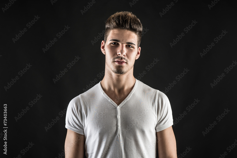 Portrait of confident young man wearing white shirt against blac