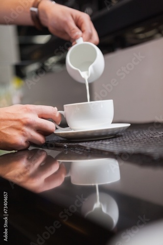 Barista pouring milk into cup of coffee