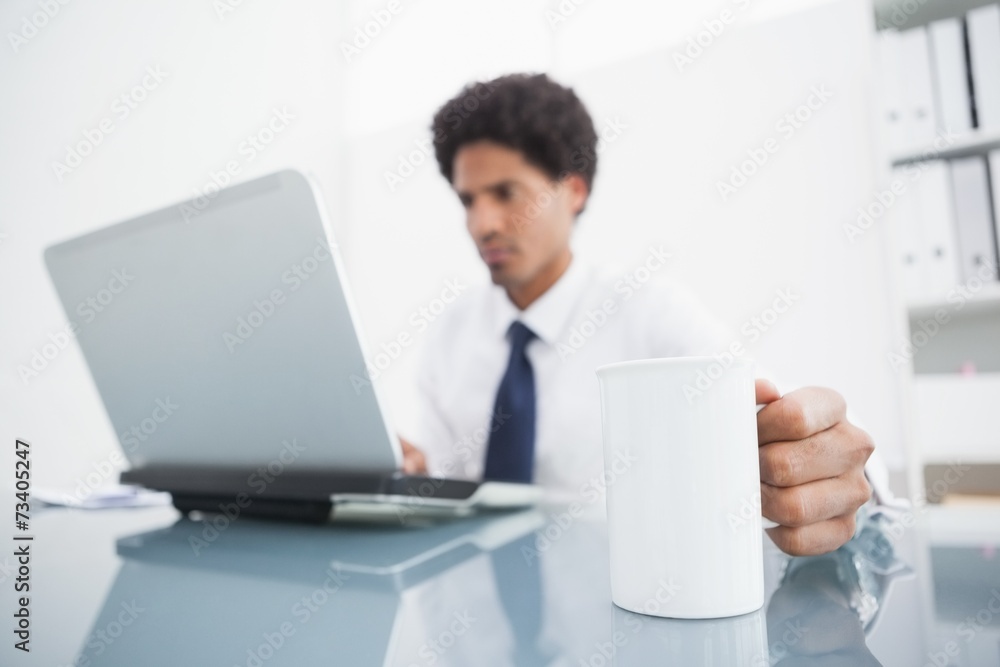 Businessman using laptop and holding mug at desk Businessman using laptop and holding mug at desk