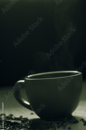 Dry tea with green leaves in cup, on burlap background