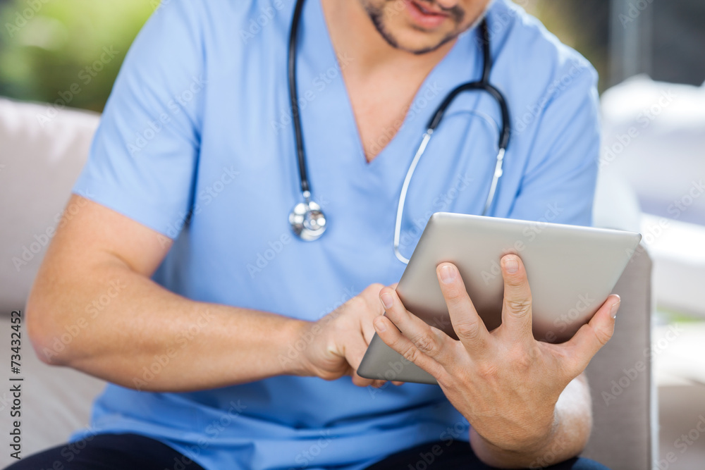 Male Caretaker Using Tablet Computer While Sitting On Couch Male Caretaker Using Tablet Computer While Sitting On Couch