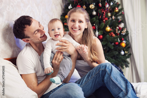 Young family with baby having fun on bed at Christmas time