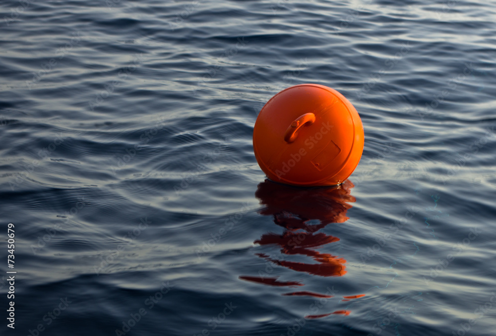 Orange fishing buoy floating in a dark blue sea at sunset