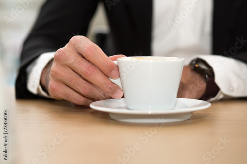 Männerhand hält Kaffeetasse auf Teller