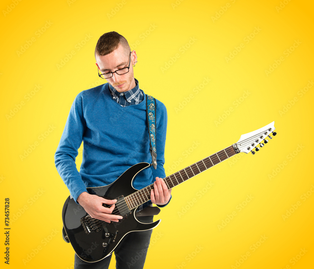 Obraz premium Young man playing guitar over yellow background