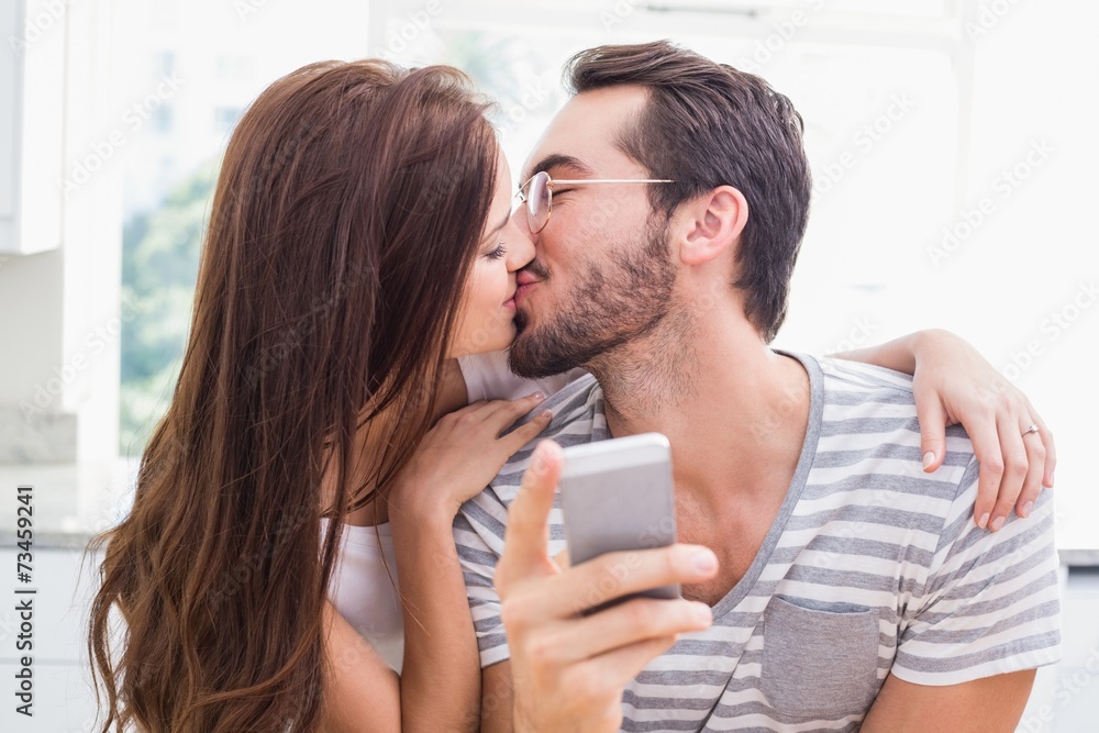 Young man using smartphone while girlfriend kisses him