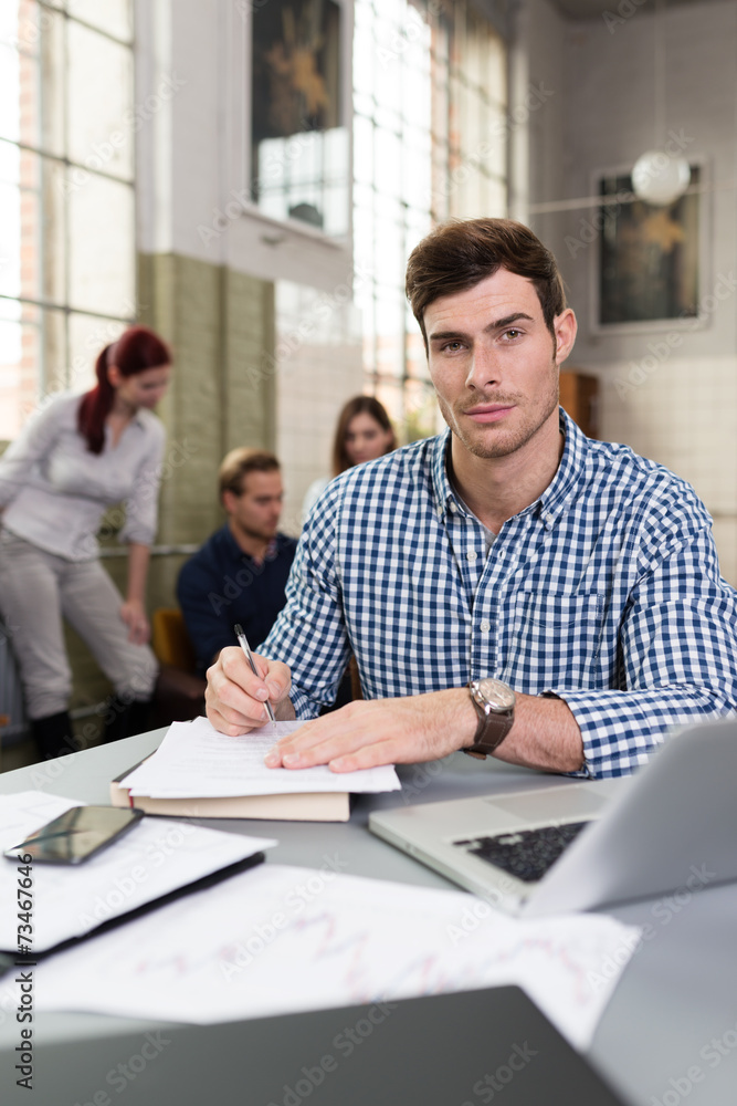 junger mann sitzt am schreibtisch mit laptop und unterlagen junger mann sitzt am schreibtisch mit laptop und unterlagen