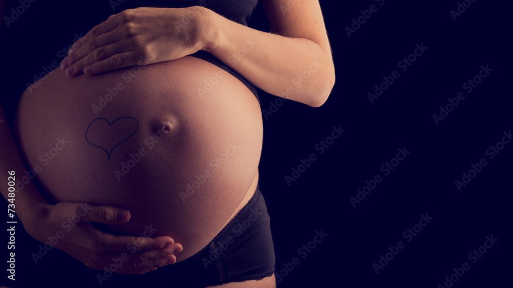 Bare swollen belly of a pregnant woman cupped by her hands Bare swollen belly of a pregnant woman cupped by her hands
