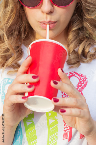 young girl in sunglasses drinking coke through a straw