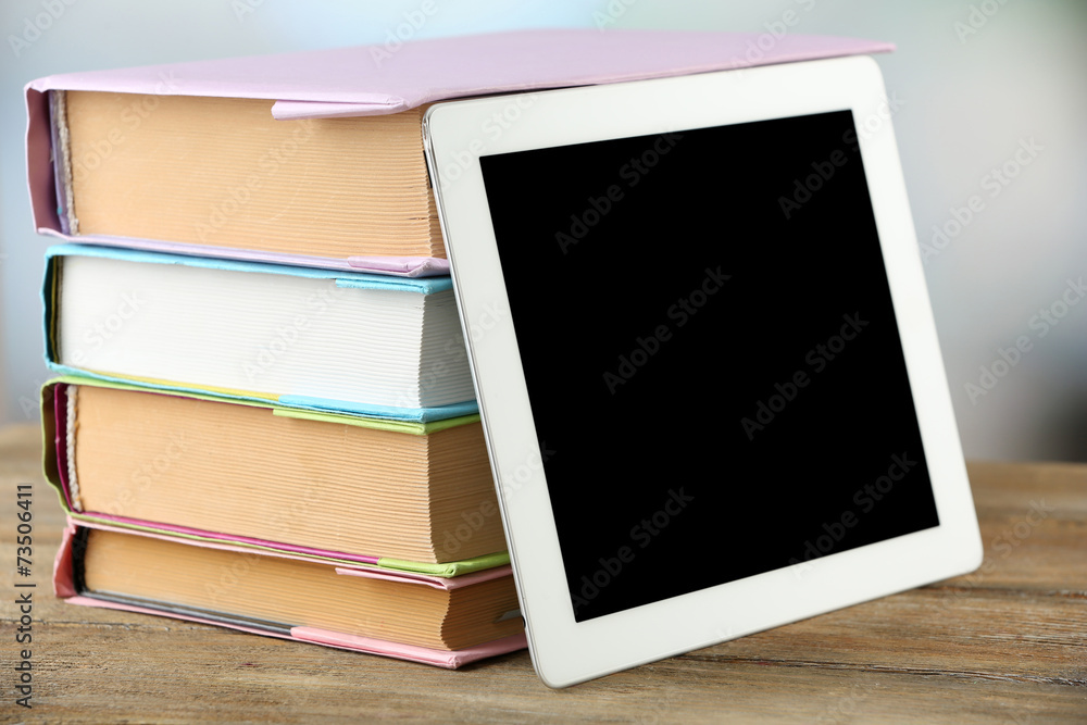 Fototapeta premium PC tablet and books on wooden table, on light background