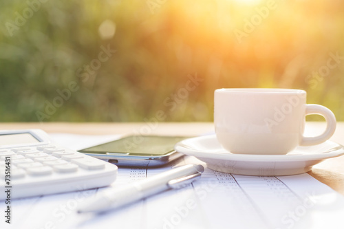 A cup of coffee on the table and calculator with number in paper