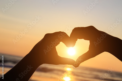 Silhouette of hands in heart symbol around the sun