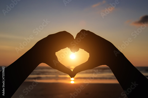 Silhouette of hands in heart symbol around the sun