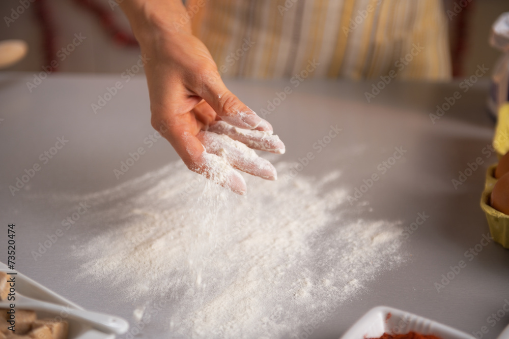 Closeup on young housewife sprinkling flour on table