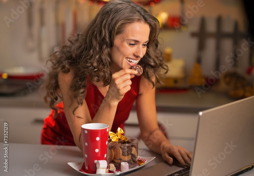 Happy young housewife with christmas snacks using laptop 