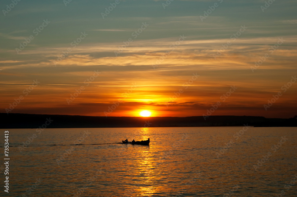 Lake sunset and little fishing boat in the distance Lake sunset and little fishing boat in the distance