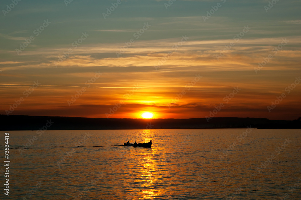 Lake sunset and little fishing boat in the distance