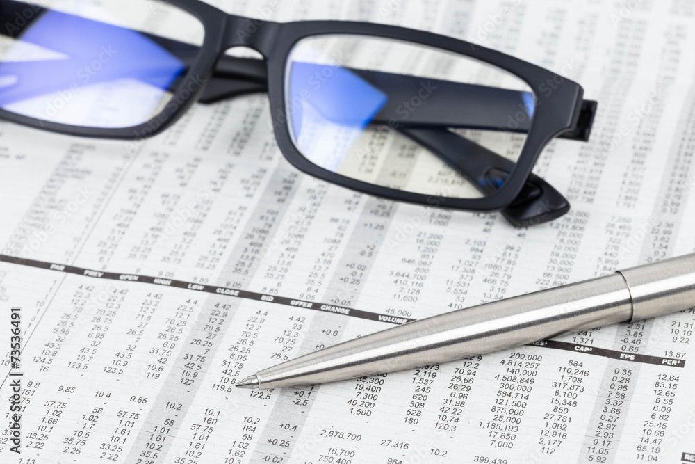 Pen and glasses rest on stock price detail financial newspaper
