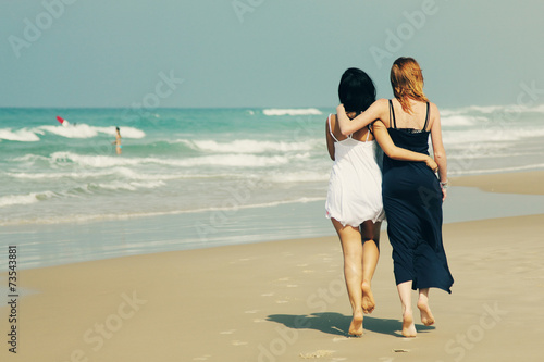 portrait of two smiling girlfriends jumping at the beach