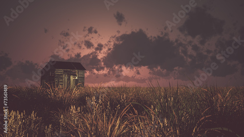 Old abandoned wooden barn on prairie at sunset with cloudy sky.