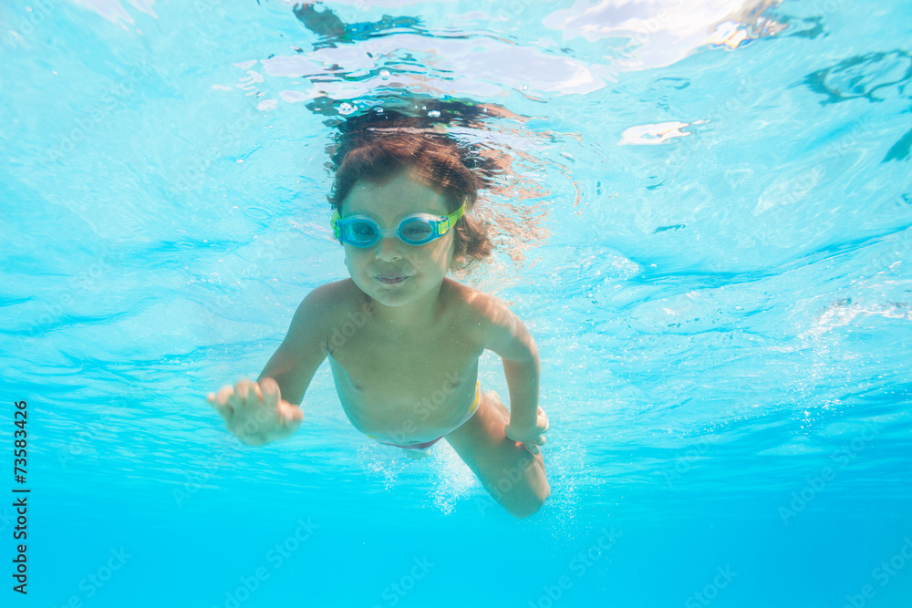 Small boy with goggles swims alone under water