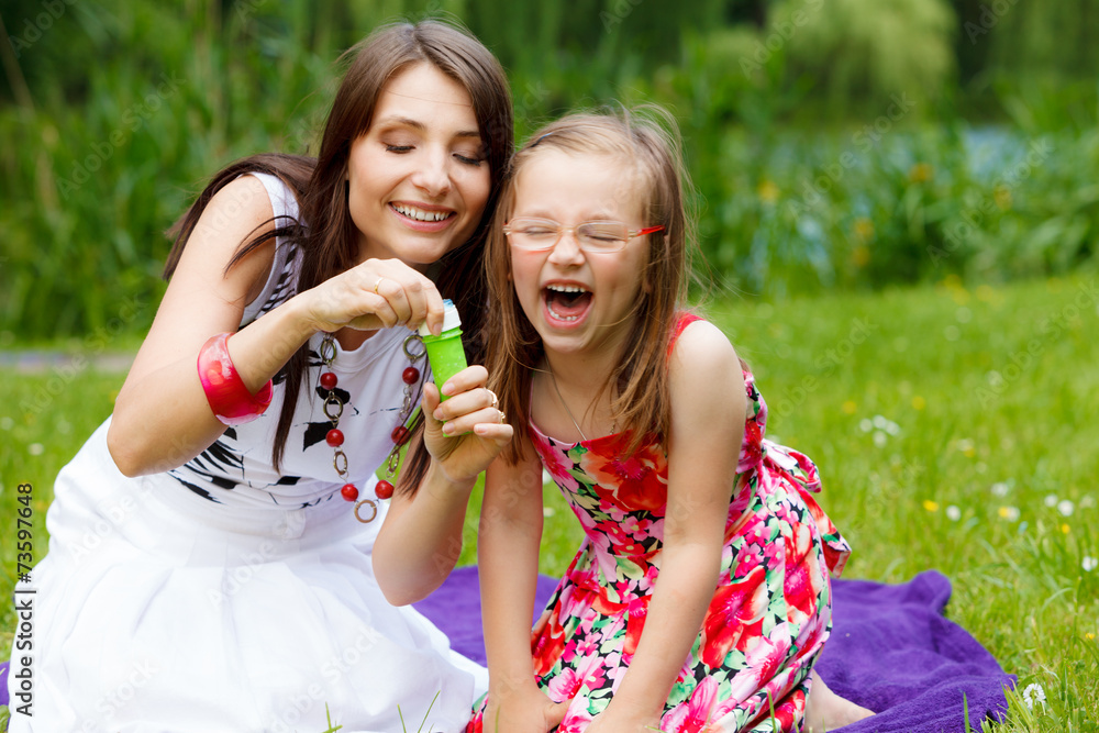Obraz premium Mother and little girl blowing soap bubbles in park.
