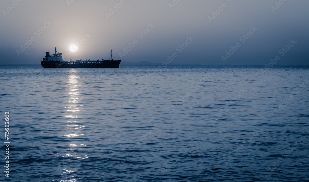 Moon rising above a sailing cargo ship