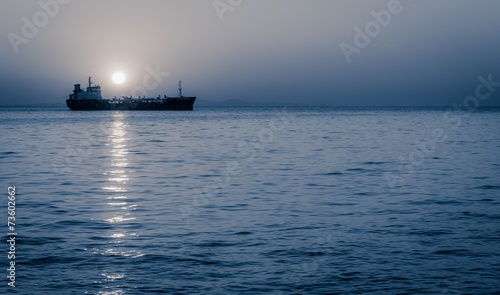 Moon rising above a sailing cargo ship © anzebizjan