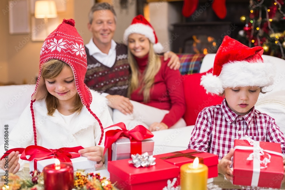 Festive little siblings opening a gift in front of their parents Festive little siblings opening a gift in front of their parents