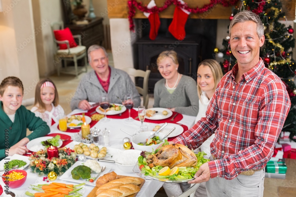Man holding turkey roast with family at dining table