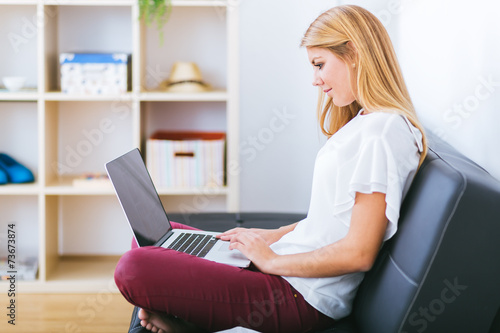Smiling young woman looking on your laptop sitting on sofa at ho