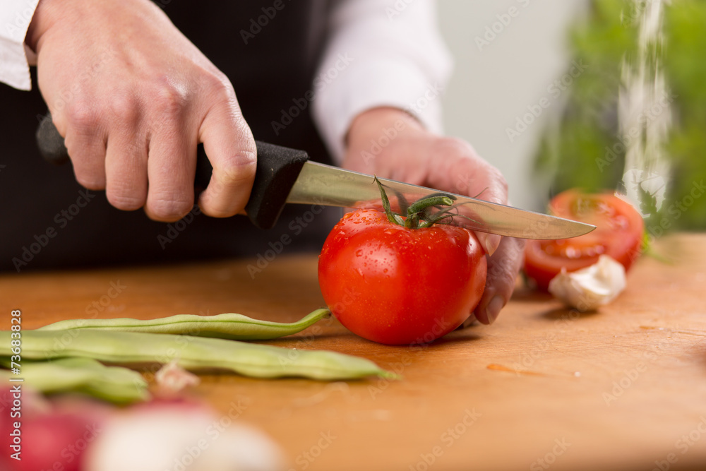 Female chopping fresh red tomato on a wooden chopping board