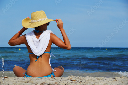 Young woman sitting on the mediterranean beach on hot summer day