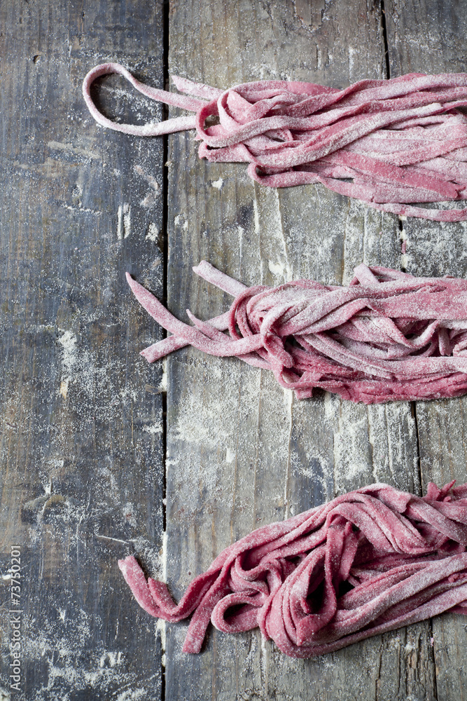 fresh homemade pasta tagliatelle with beetroot on wooden table