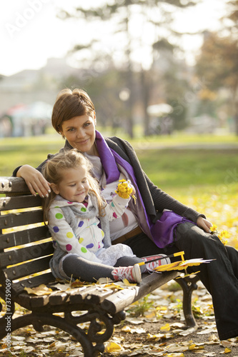 Happy Family Mother and Daughter Sitting on Bench In Park