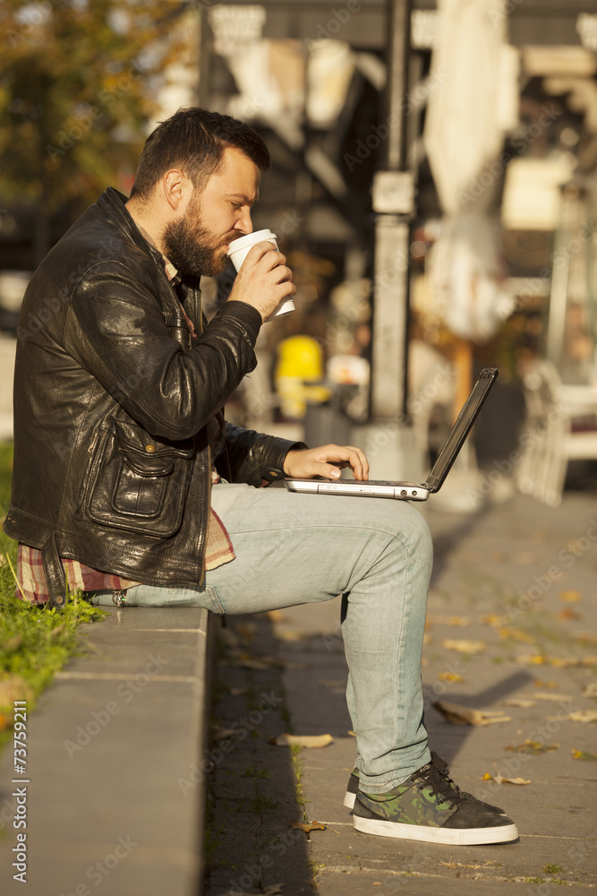 Man Using Laptop Computer and Drinking Coffee From To Go Cup