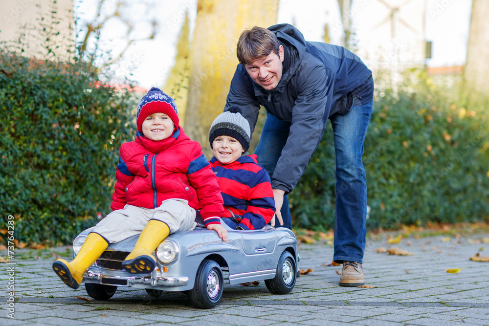 Two happy sibling boys and father playing with big old toy car, Two happy sibling boys and father playing with big old toy car,