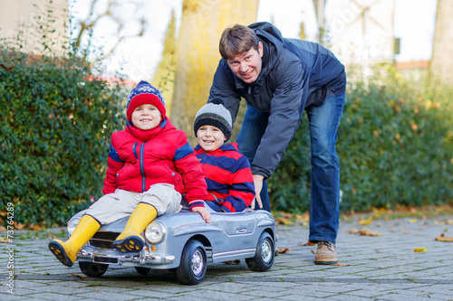 Two happy sibling boys and father playing with big old toy car,